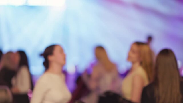 Fashion show with blurred audience. Silhouetted attendees in front row captured with blurred background and ambient lighting