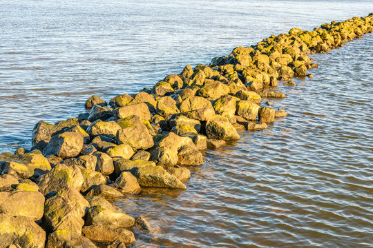 A breakwater made of boulders in a Dutch river. The photo was taken on a sunny day in winter.