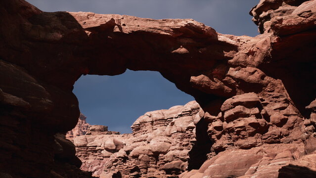Hikers venture through a breathtaking landscape, admiring the towering red rock formations and a remarkable arch. The sun casts warm light on the rugged terrain, creating a surreal atmosphere.