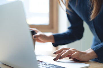 Fototapeta premium Close up of business woman working on laptop, surfing the net and holding a cup of coffee at office, corporate business concept