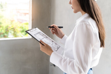 Asian inspector checking structure of new property and taking note in the clipboard for review and...