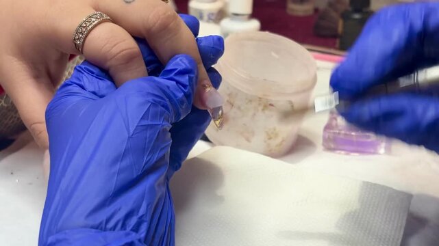 Technician applying acrylic or gel extension with glitter design on long artificial nails.