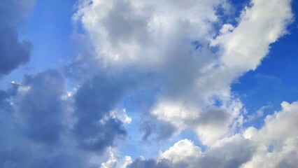 Obraz premium Background of bright clouds shrouded in dark evening clouds with blue sky. Blue sky with light white clouds illuminated by the sun in early spring