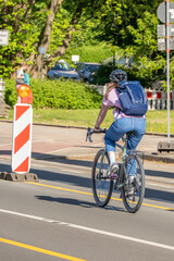 Fototapeta premium Cyclist riding along a protected urban bike lane on a sunny day, sustainable city transport with green trees (Acer sp., Tilia sp.) lining the street.