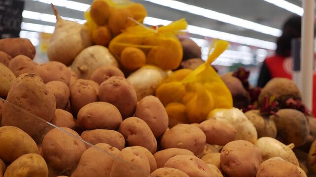 Potatoes lie in a large supermarket vegetable display among other produce, filling the counter with earthy root vegetables. Grocery shopping.