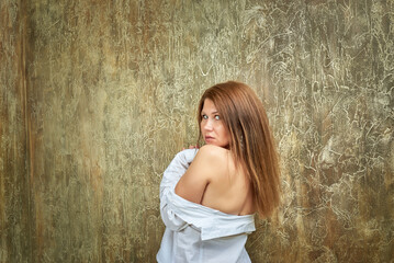 Fototapeta premium Sexy young woman in a white shirt is depicted on a textured brown background. Her long straight hair has a brownish tint.