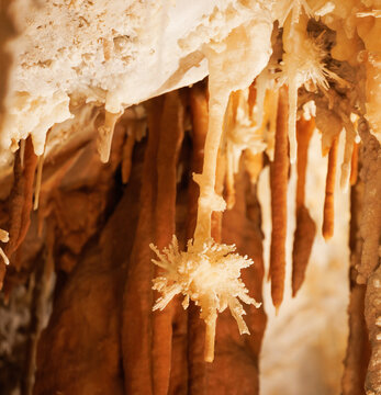 L'image repr&eacute;sente l'int&eacute;rieur d'une grotte avec des stalactites et stalagmites de couleur orange-brun, ainsi que des formations cristallines en forme d'&eacute;ventail.