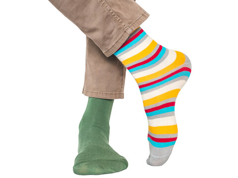 Man wearing mismatched colorful striped and green socks and light brown pants without shoes. Casual fashion, individuality and self-expression concept. Studio shot on isolated background, closeup