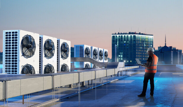 HVAC inspection, building maintenance. Technician with laptop checks rooftop air conditioning units and ventilation systems of commercial building during technical monitoring.