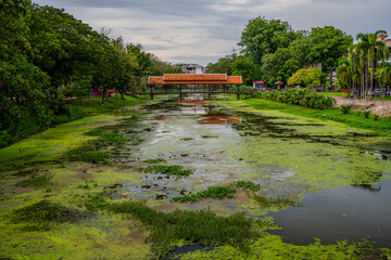 Fototapeta premium Covered wooden bridge over algae-filled moat in Siem Reap