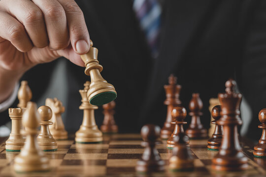 Man's hand moving white king chess piece on wooden board, strategy game concept