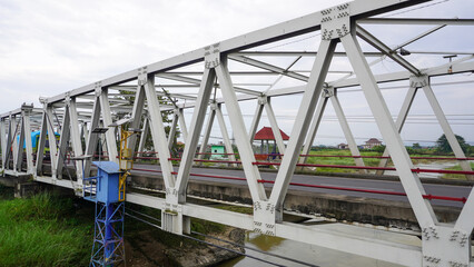 Steel bridge over river in rural landscape with cloudy sky
