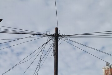 Fototapeta premium Tangled Utility Pole With Overhead Wires Against Cloudy Sky in Urban Neighborhood