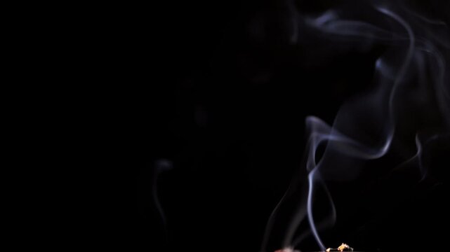 Thin wisps of white smoke gracefully curl and billow before fading into a dark background. Concept of magical atmosphere, spiritual meditation, and abstract floating vapor forms. Slow motion.