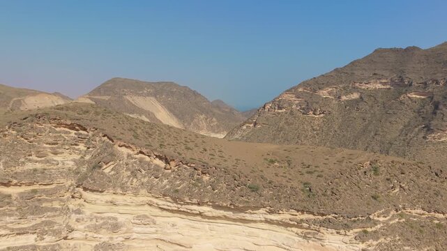 Aerial view of stratified rock formations and a winding road through an arid mountain valley near the coast in Iran.