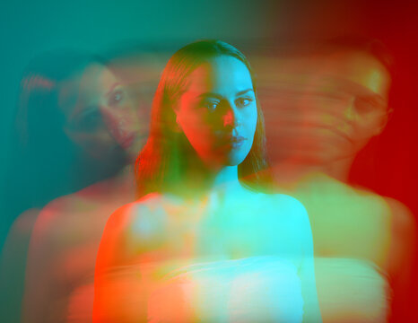 Close up studio portrait of female model face with creative neon studio lighting and slow shutter speed creating colourful blue and red 3d surreal effect.