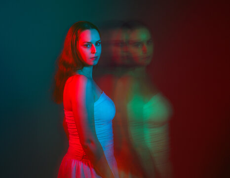 Close up studio portrait of female model face with creative neon studio lighting and slow shutter speed creating colourful blue and red 3d surreal effect.
