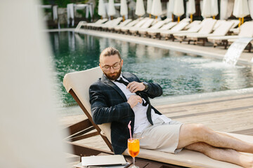 Fototapeta premium Businessman relaxing by the pool after work, loosening his tie