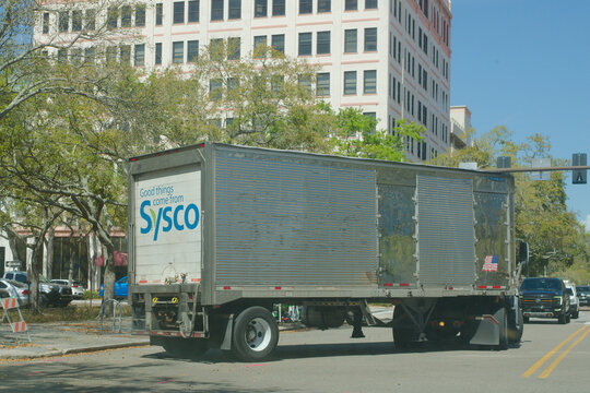 White Sysco Food Semi Truck Making A Turn On City Street With American Flag Trailer Sticker. Editorial Use Only March 6, 2026 St. Petersburg, FL USA. Other cars waiting at the intersection under clear