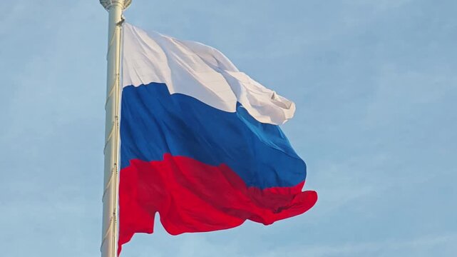A flagpole with the flag of the Russian Federation waving gracefully in the wind, set against a bright sky. Patriotic imagery.