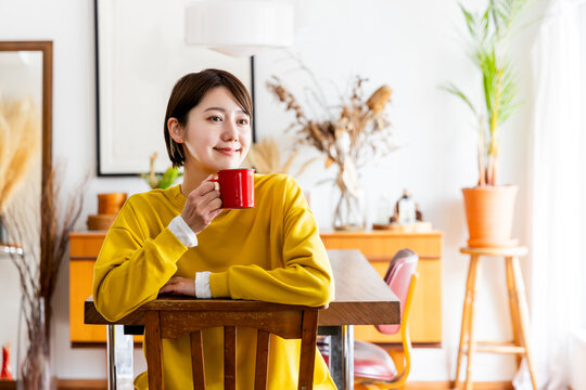 椅子に反対向きに跨いで座りコーヒーを飲む女性