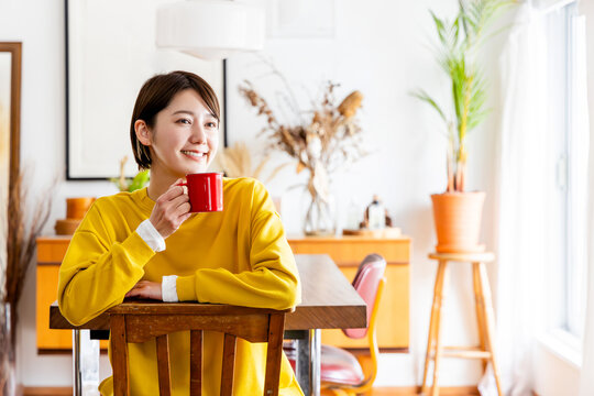 椅子に反対向きに跨いで座りコーヒーを飲む女性
