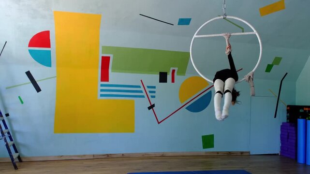Nine year old girl practices aerial gymnastics tricks on aerial hoop in sports school with safety harness and elastic bandages on legs, slow motion, strength flexibility training