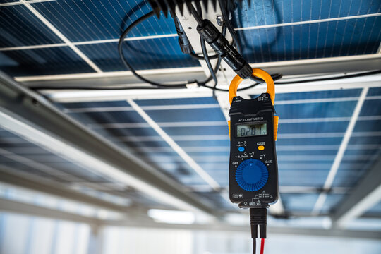 Digital clamp meter connected to photovoltaic solar panel wiring measuring electrical current during solar power system inspection and renewable energy monitoring