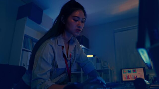 Serious Asian Woman Computer Programmer Coding Software Developer Working Late Night Office Focused On Screen Writing Code For Deadline Project Under Cinematic Dark Blue Room Light