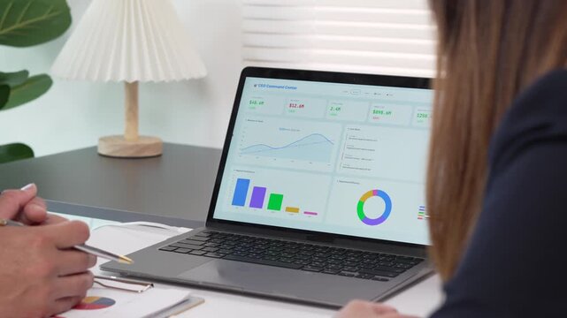 Business executives reviewing data analytics and financial charts on a laptop during an office meeting.