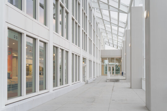 Contemporary indoor walkway under glass canopy with repeating window grid, clean public corridor for office, hospital, or retail facility branding