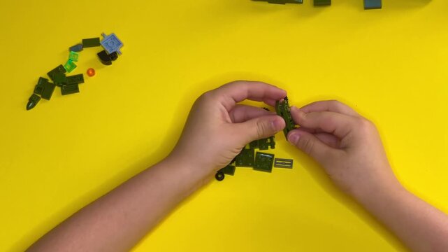 Close-up of children's hands building with building blocks on a bright yellow background