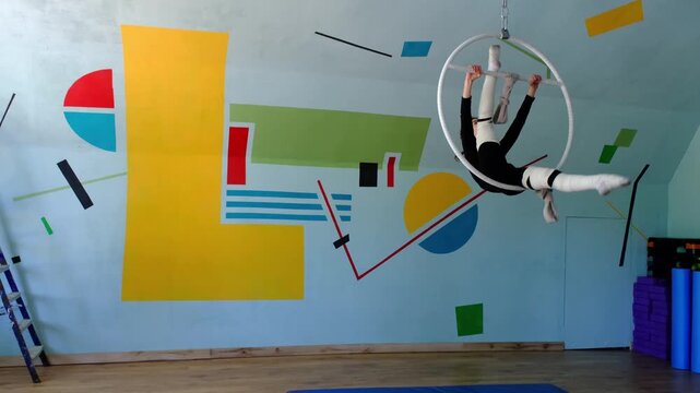 Nine year old girl practices aerial gymnastics tricks on aerial hoop in sports school with safety harness and elastic bandages on legs, slow motion, strength flexibility training