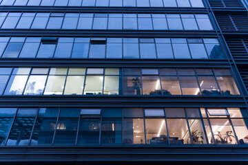 Obraz premium Modern office building at night with illuminated windows showing interior workspaces and office activities