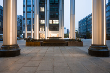 Modern architectural plaza with illuminated columns and glass facade at dusk