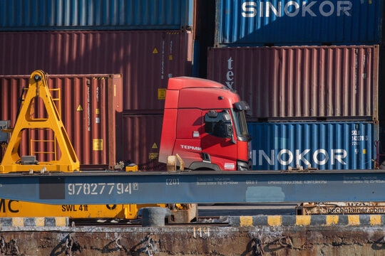 Vladivostok, Russia - February 16, 2026: Red truck parked beside shipping containers at a freight terminal with visible brand names and industrial equipment in the background