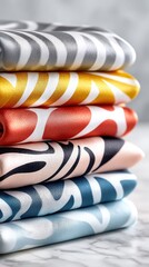 Fototapeta premium Neatly stacked pile of six folded textiles rests on white marble. Each fabric features a unique bright color gray, yellow, red, pink, blue, and light blue, adorned with a repeating white wavy pattern