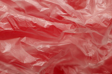 Fototapeta premium ​A macro shot demonstrates the complex abstract texture of a thin red plastic bag with numerous wrinkles and creases. The detailed polyethylene surface creates a play of light and shadow, highlighting