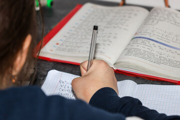 A student is focused on solving mathematical equations in a notebook, using a textbook for preparation. The shot conveys an atmosphere of learning, homework, and intellectual work, focusing on the han