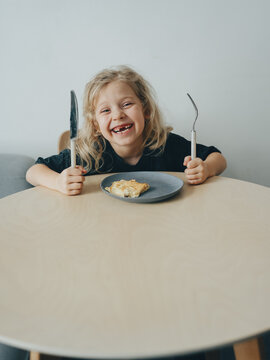 A child with missing front teeth enjoys eating at the table with a fork and spoon. Minimalism is an emotion for dentists.
