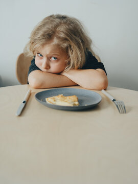 A child at the table is disappointed that he will have to eat unpleasant food. Sad child