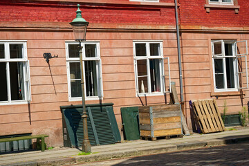 Old lamp by apartment block with open windows and pallets leaning. © Holger