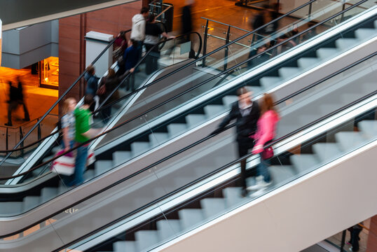 Shoppers (blurred due to movement) take the escalators in a shopping centre/mall.