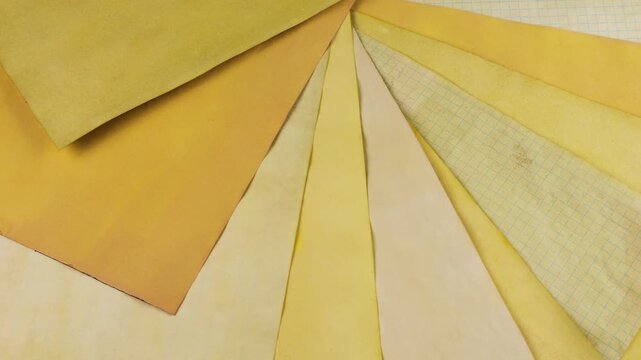 Rotating collection of handmade paper sheets showcasing a variety of yellow and ochre shades achieved through natural coloring matter. The vintage textured surface of the aged pages.