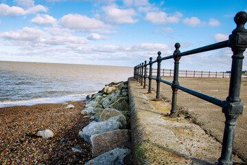 Wide Angle View of an Empty Coastal Promenade with Black Metal Railings and Shingle Beach Under a Cloudy Blue Sky
