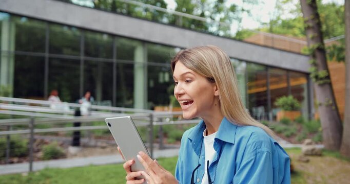 Woman user customer standing in urban street using digital tablet, get amazing sale offer winning online bid, feel ecstatic reading great online news at outside