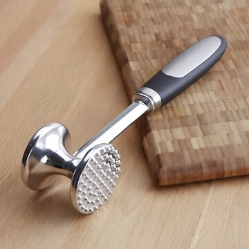 Meat tenderizer with black handle on wooden cutting board surface