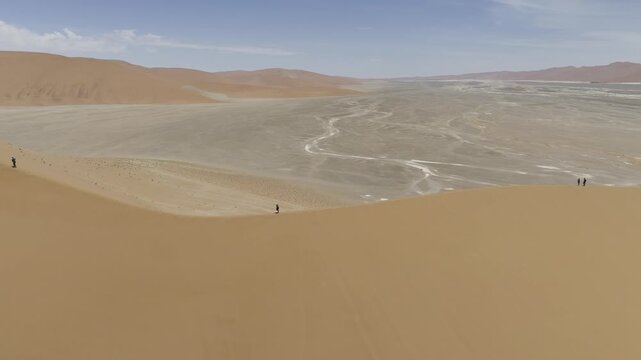 Drone orbits from profile shot of Dune 45 to perpendicular with the ridge as hikers climbs on sunny day in Sossusvlei, Namibia