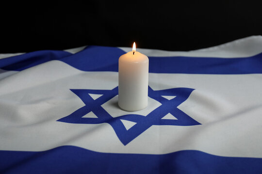 Holocaust Remembrance Day. Burning candle on flag of Israel against dark background, closeup