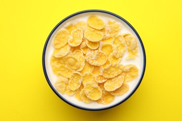 Tasty corn flakes with milk in bowl on yellow table, top view